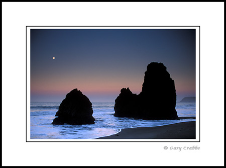 Moonset at dawm over rocks and ocean, Rodeo Beach, Marin County Coast, California