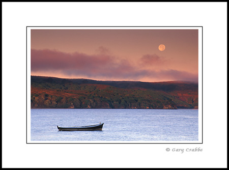 Full moon setting at dawn over lone boat in Tomales Bay, Marin County Coast, California