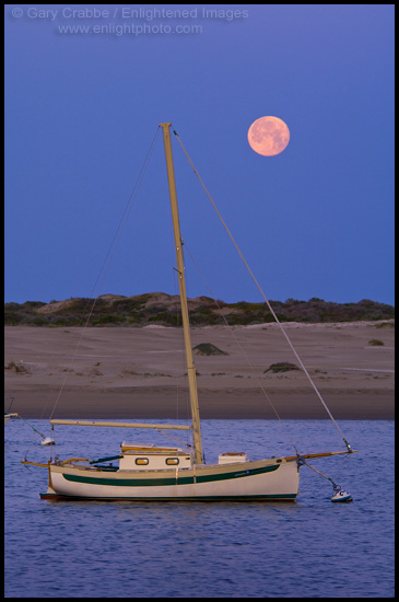 Full moon setting at dawn over sailboat, Morro Bay, California
