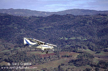 Small single engine fixed wing airplane (Maule) over wooded hills of Sonoma County, California