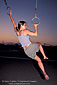 Athletic woman excersises by swinging on rings in evening at Santa Monica Beach, Santa Monica, California