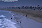 People wade in ocean surf at sunset below evening fog, near Balboa Pier, Balboa Island, Newport Beach, California