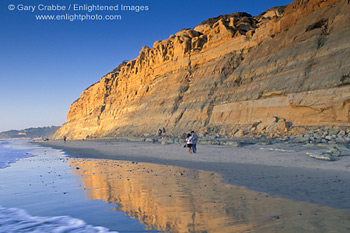 People walking on sand and golden cliffs reflected in water, Torrey Pines State Beach, near La Jolla, San Diego County Coast, California