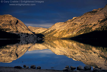 Sunlight on mountains sneaks through storm clouds at sunset over Tenaya Lake, Tioga Pass Road, Yosemite National Park, California