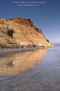 Couple walking on beach below golden sandstone cliffs, Torrey Pines State Park, San Diego County, California