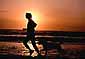 Female jogger and canine companion running along beach at sunset, near Eureka, Humboldt County, California