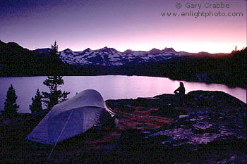 Hiker on rock at backpackers wilderness tent camp below the Lyell Crest mountains in evening, High Sierra, California