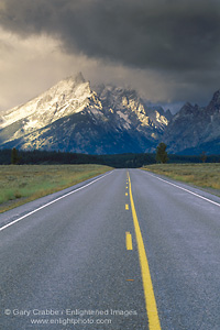 Picture: Straight two lane road below snow covered mountains and storm clouds, Grand Teton National Park, Wyoming