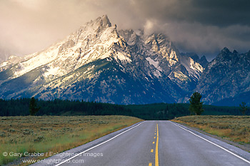 Picture: Straight paved two lane road below snow capped mountains and clearing storm, Grand Teton National Park, Wyoming