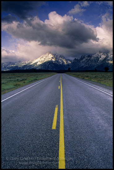 Straight road below mountain range dusted by first snow of fall, Grand Teton National Park, Wyoming