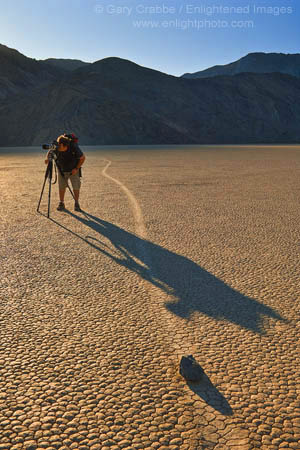Photographer next to tracks left by mysterious moving rocks on the dried flat mud at the Racetrack Playa, Death Valley National Park, California