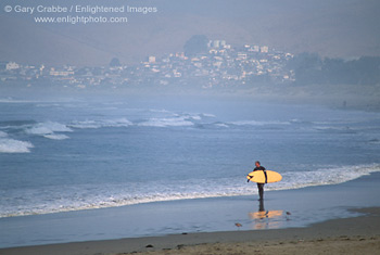 Surfer walking on sandy beach looking at waves, near Morro Bay, Central Coast, California; Stock Photo photography picture image photograph fine art decor print wall mural gallery