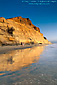 Couple walking together on beach below golden cliffs reflected in water, Torrey Pines State Beach, San Diego County, Southern California Coast