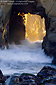 Sunset light and crashing wave through keyhole in coastal rock, Big Sur, California