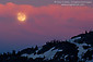 Full moon rising trough red clouds over mountain ridge at sunset, Desolation Wilderness, California
