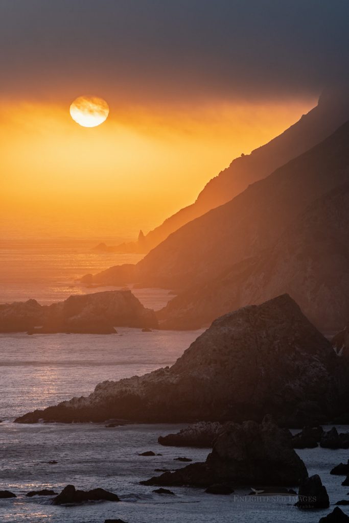 Photo: Setting sun dips below coastal clouds over the headland cliffs at Point Reyes National Seashore, Marin County, California