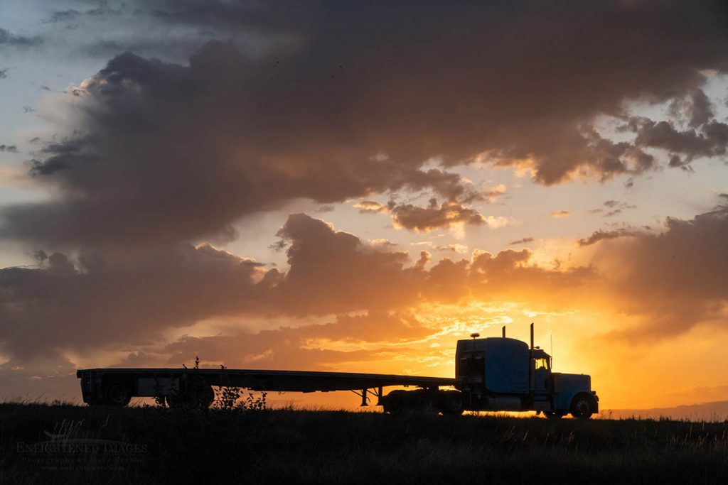 Photo Picture of Sunrise and clouds in sky behind big rig truck and flatbed trailer off highway in rural Kansas