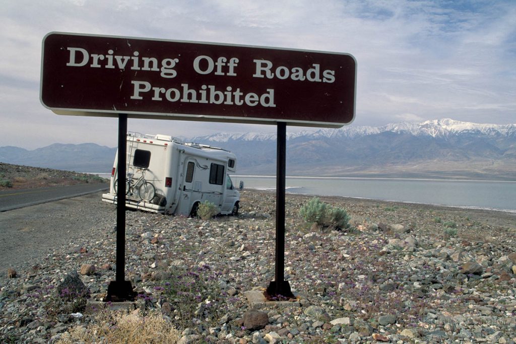 Photo picture of Driving off road prohibited Tourist RV tavel Camper stuck in desert rocks after drive offroad next to warning sign, near Badwater, Death Valley National Park, California